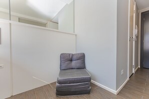 Quarto moderno com um banco estofado cinza encostado na parede, uma porta à direita e uma escada ao fundo.