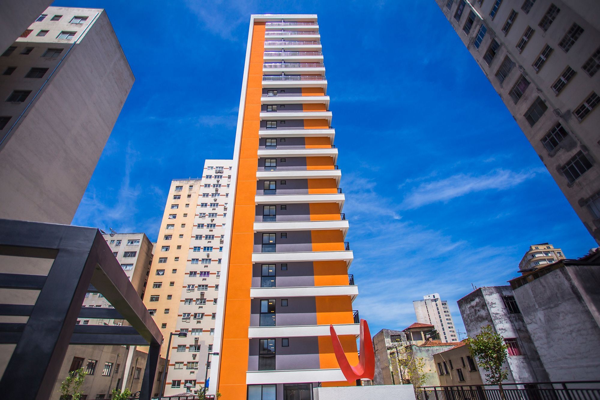 Un edificio alto y moderno con un llamativo diseño de color naranja y blanco, rodeado de otros edificios.