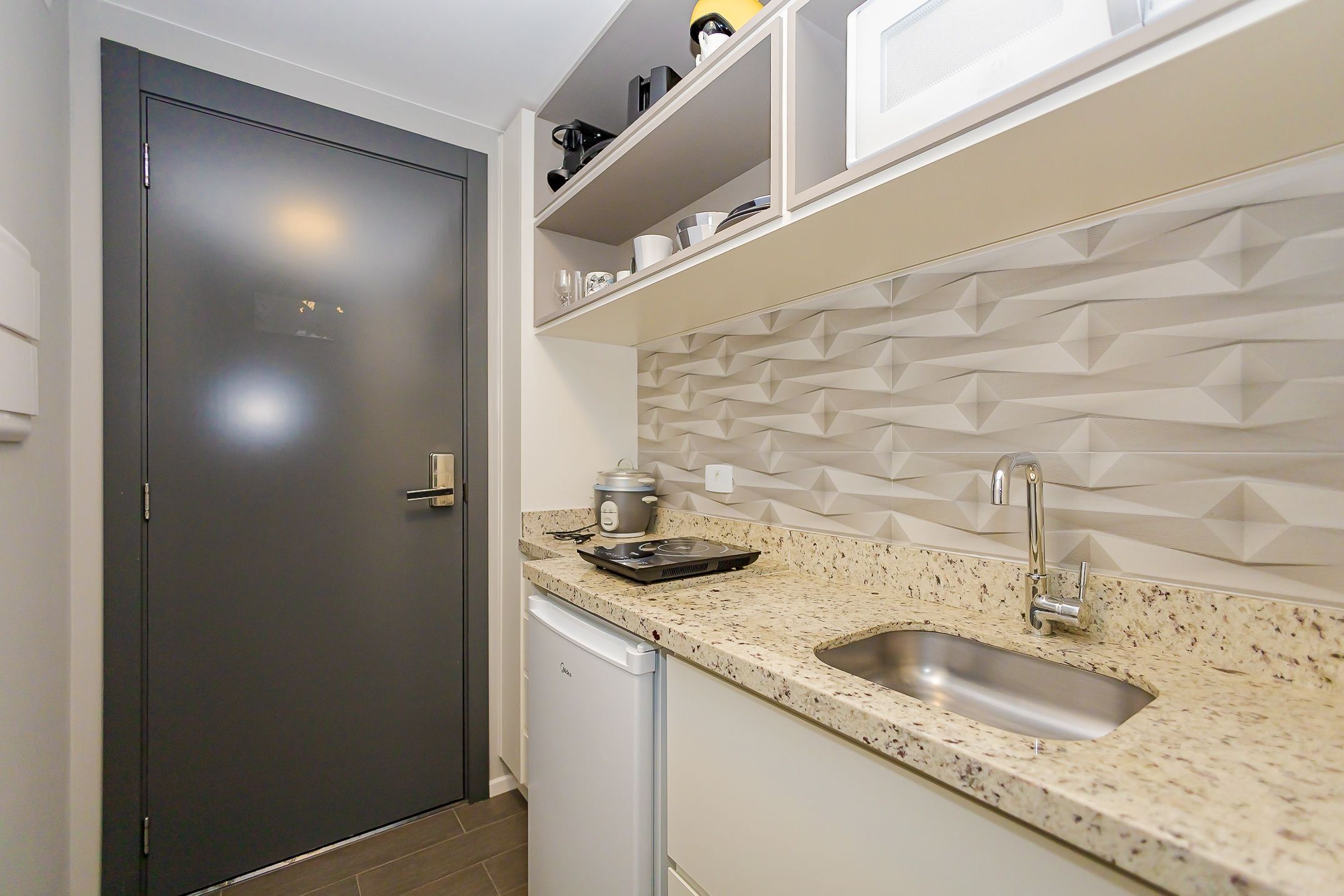 A modern kitchen with a dark door, a built-in dishwasher, a granite countertop, and a geometric backsplash.