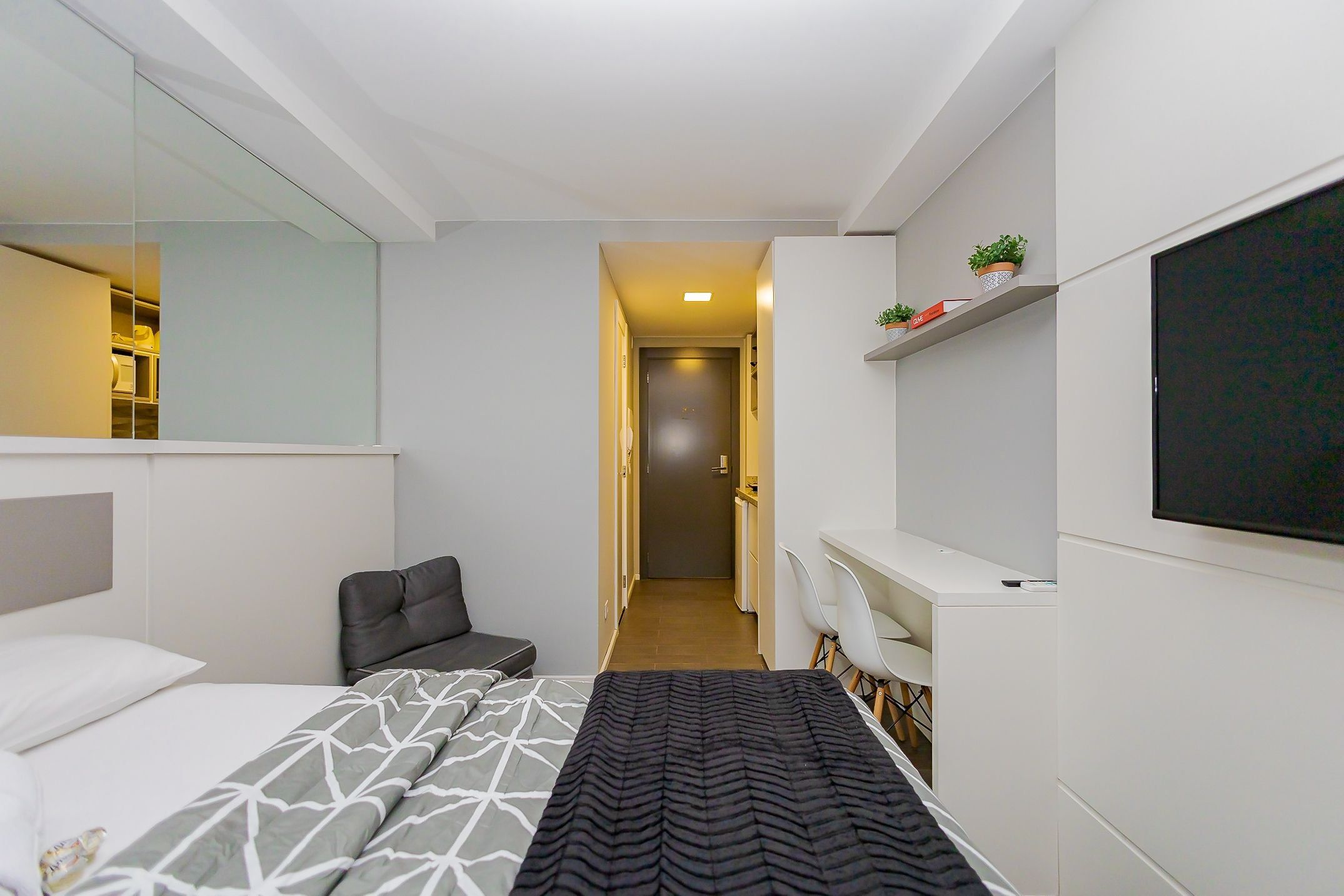 Quarto de hotel moderno com cama, área de estar, escrivaninha e televisão.