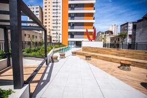 Terraço ao ar livre com piso de madeira, áreas de estar e vista para edifícios próximos.