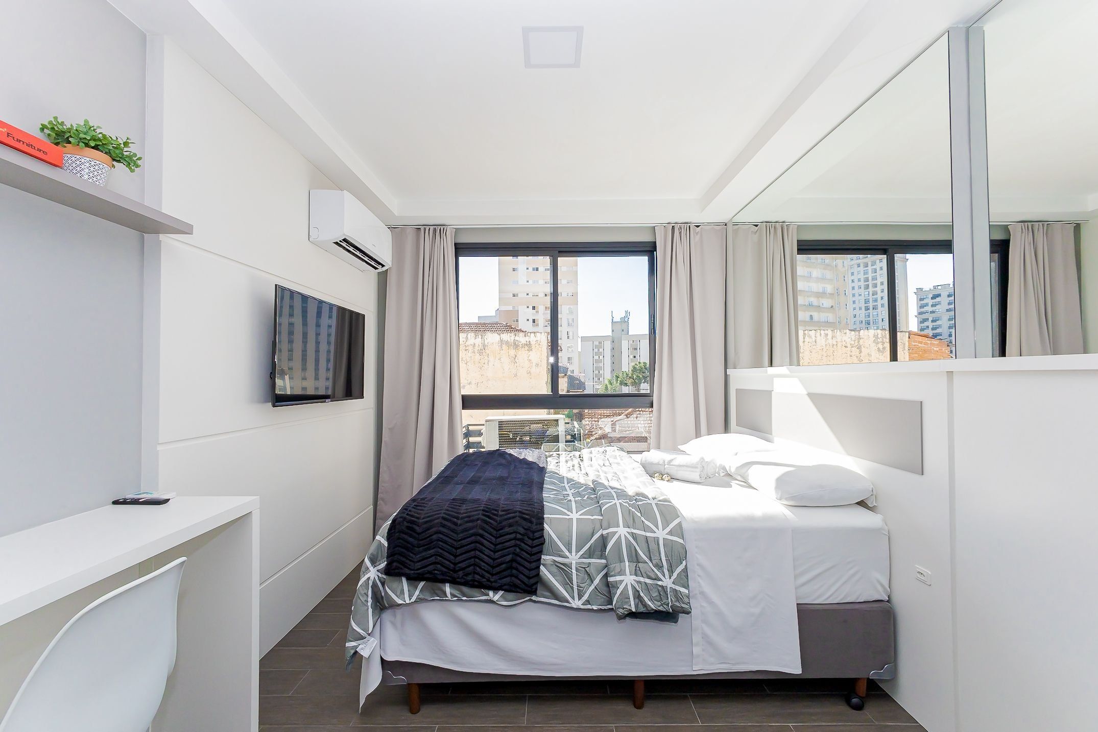 Un dormitorio moderno con cama, televisión, escritorio y ventana con cortinas.