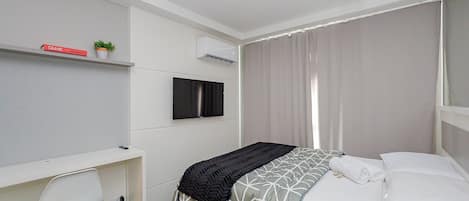 A modern bedroom with a bed, a desk, a chair, a TV, and a potted plant.