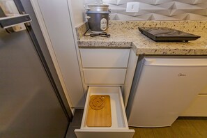 Cozinha com bancada, uma panela de cozimento lento, máquina de lavar louça e uma gaveta com tábua de corte.
