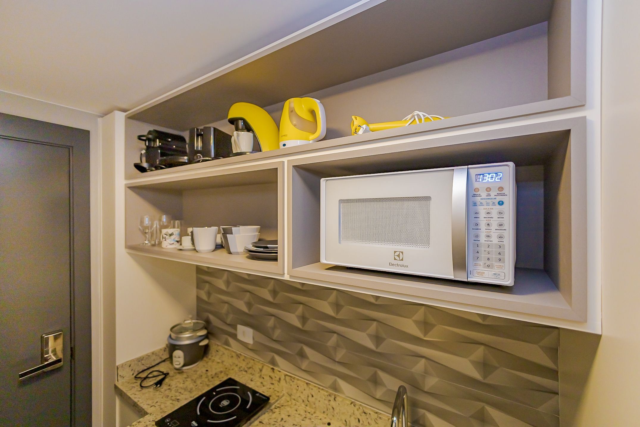 A kitchen with a microwave, a coffee maker, and a kettle on the countertop.