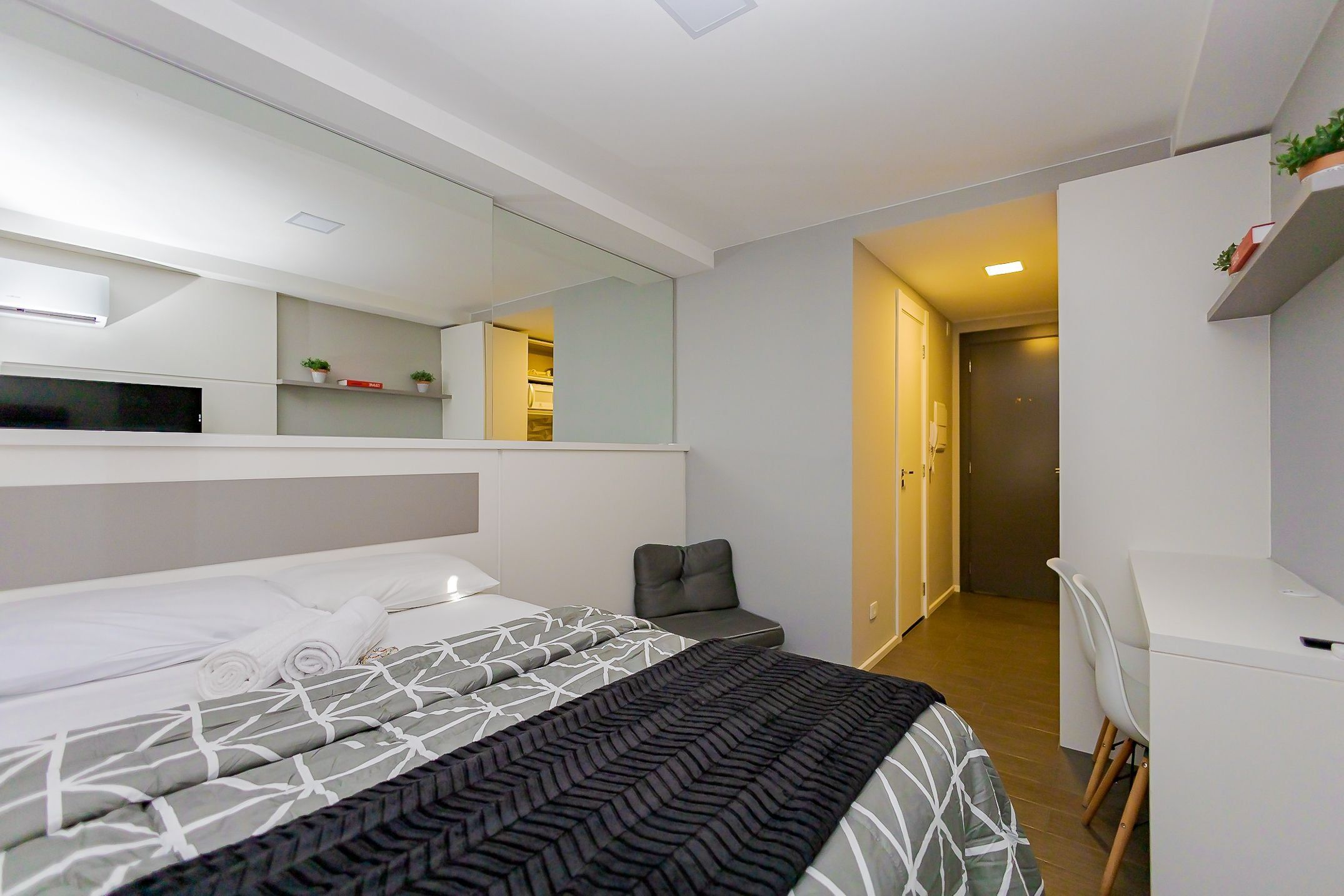 A modern hotel room with a large bed, a desk, and a walk-in closet.