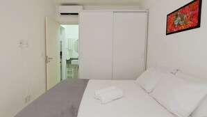 Une chambre à coucher avec un lit, des rideaux blancs, une armoire blanche et un appareil de climatisation.