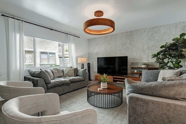 Un salon moderne avec un canapé gris, une table basse et un grand téléviseur à écran plat.