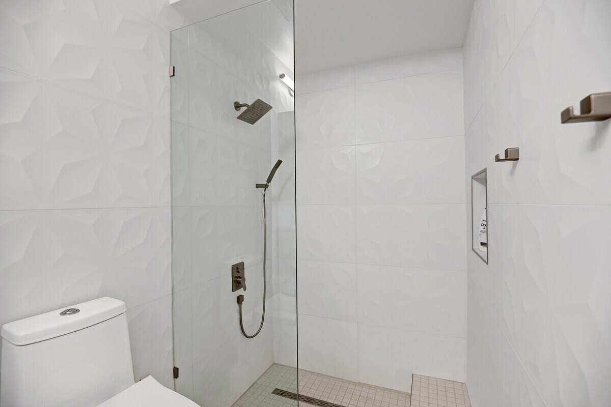 Une salle de bain moderne avec une douche à parois de verre, des murs recouverts de carrelage blanc et des toilettes.