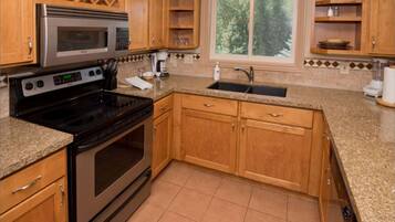 A kitchen with wooden cabinets, a stainless steel microwave, a black stove, a sink, and a window with a view of trees.