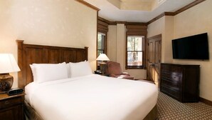 A hotel room with a large bed, a desk with a lamp, a chair, a dresser, and a TV mounted on the wall.