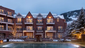 A multi-story hotel with a pool in the foreground, featuring balconies and a view of snow-covered mountains.