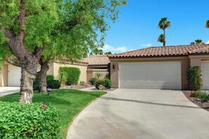 A residential driveway leading to a house with a garage, surrounded by well-maintained landscaping and a clear sky. - Southern Exposure-Large Patio-BBQ-Dogs OK-V3659 (Palm Desert)