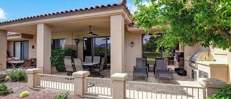 A covered patio area with outdoor seating, a ceiling fan, and a barbecue grill.