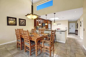 Un comedor con mesa y sillas de madera, una cocina al fondo y vistas al exterior.