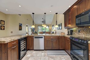 A kitchen with granite countertops, wooden cabinets, stainless steel appliances, pendant lighting, and a large island with seating. - Southern Exposure-Large Patio-BBQ-Dogs OK-V3659 (Palm Desert)