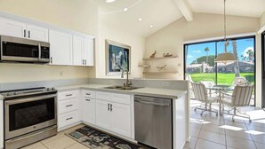 Una cocina moderna con muebles blancos, electrodomésticos de acero inoxidable y vistas a un patio con mobiliario exterior.