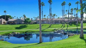 Un campo de golf con un estanque, palmeras y un club de campo al fondo.