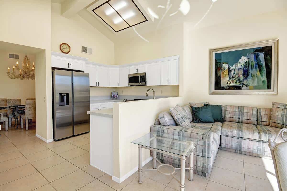 A modern kitchen with white cabinets, a stainless steel refrigerator, and a microwave. There's a glass coffee table and a plaid sofa in the living area.