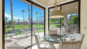 Una habitación moderna con una mesa y sillas de vidrio, ventanas amplias que ofrecen vista a un campo de golf y palmeras.