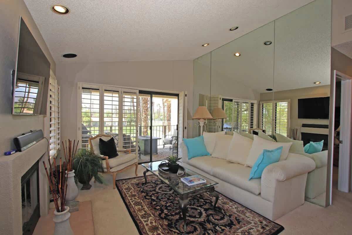A living room with a white sofa, a glass coffee table, a fireplace, and a large mirror.