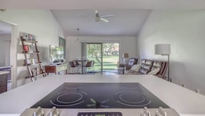 Una cocina moderna con una isla central, comedor con sillas, un sofá y un ventilador de techo.
