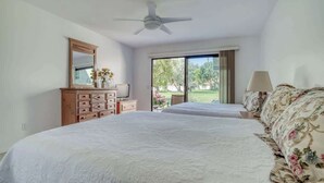 Un dormitorio con una cama grande, un aparador, un espejo, un ventilador de techo y una ventana con vistas a la vegetación.