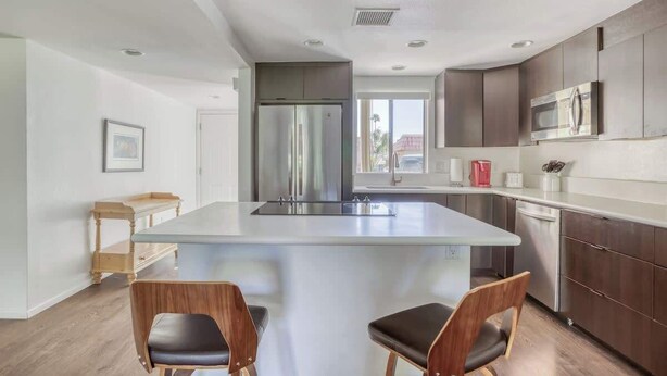 Una cocina moderna con una isla central, electrodomésticos de acero inoxidable y sillas de madera.