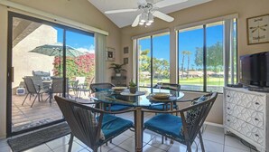 Un coin repas avec une table et des chaises en verre, un ventilateur de plafond et une vue sur l’extérieur.