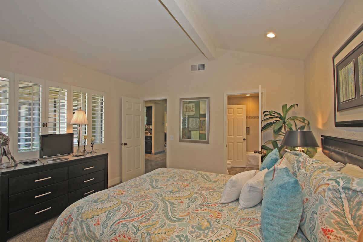 A bedroom with a bed, a dresser, a television, and a plant.