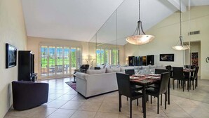 A spacious living area with a large sofa, dining table, and chairs. There are large windows with a view of greenery outside. - Spacious-Dogs Ok-Great Views-VB887 (Palm Desert)