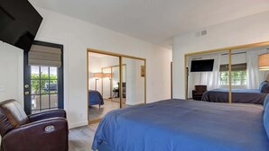 Een hotelkamer met een groot bed, een leren fauteuil, een televisie en een schuifdeur naar een balkon.