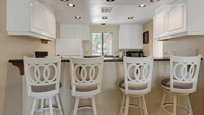 A kitchen with white cabinets, a central island with bar stools, and recessed ceiling lights. - Great Golf Condo with Access to Resort Amenities (Palm Desert)