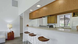 Una cucina moderna con mobili in legno, una zona bar con sgabelli e una finestra con persiane.