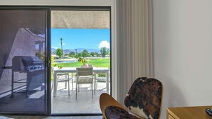 Una stanza con una porta scorrevole in vetro che dà su un patio esterno. Il patio presenta un barbecue, un tavolo con sedie e vista su un paesaggio verde con montagne sullo sfondo.