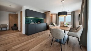 Une cuisine moderne avec des meubles de couleur sombre, une table à manger en bois et un luminaire suspendu.