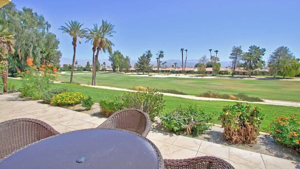Eine Terrasse mit Korbmöbeln und Blick auf einen Golfplatz.