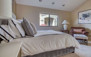 Un dormitorio con una cama grande, una mesita de noche, una silla, un ventanal y un cuadro en la pared.