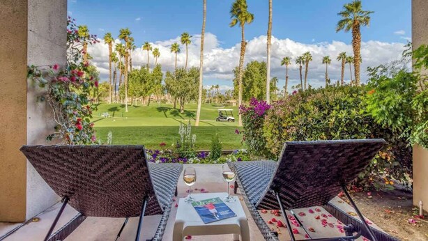 A balcony with wicker chairs and a table, overlooking a golf course with palm trees and a clear sky. - Patio-BBQ-4th Green-VB925 (Palm Desert)