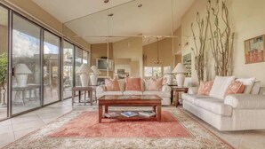 A spacious living room with a large glass door leading to a patio, a beige sofa set, a coffee table, and a chandelier. - Patio-BBQ-4th Green-VB925 (Palm Desert)