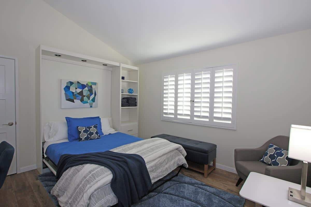 Une chambre à coucher comprenant un lit, des tables de chevet, un banc, une chaise, un bureau et une fenêtre avec des stores.