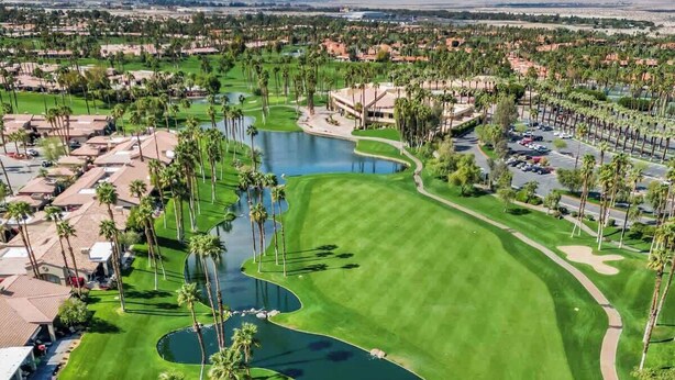 A golf course with a pond, palm trees, and a view of a cityscape in the background. - Moutain and Fairway Views-Walk to Pool-V3986 (Palm Desert)