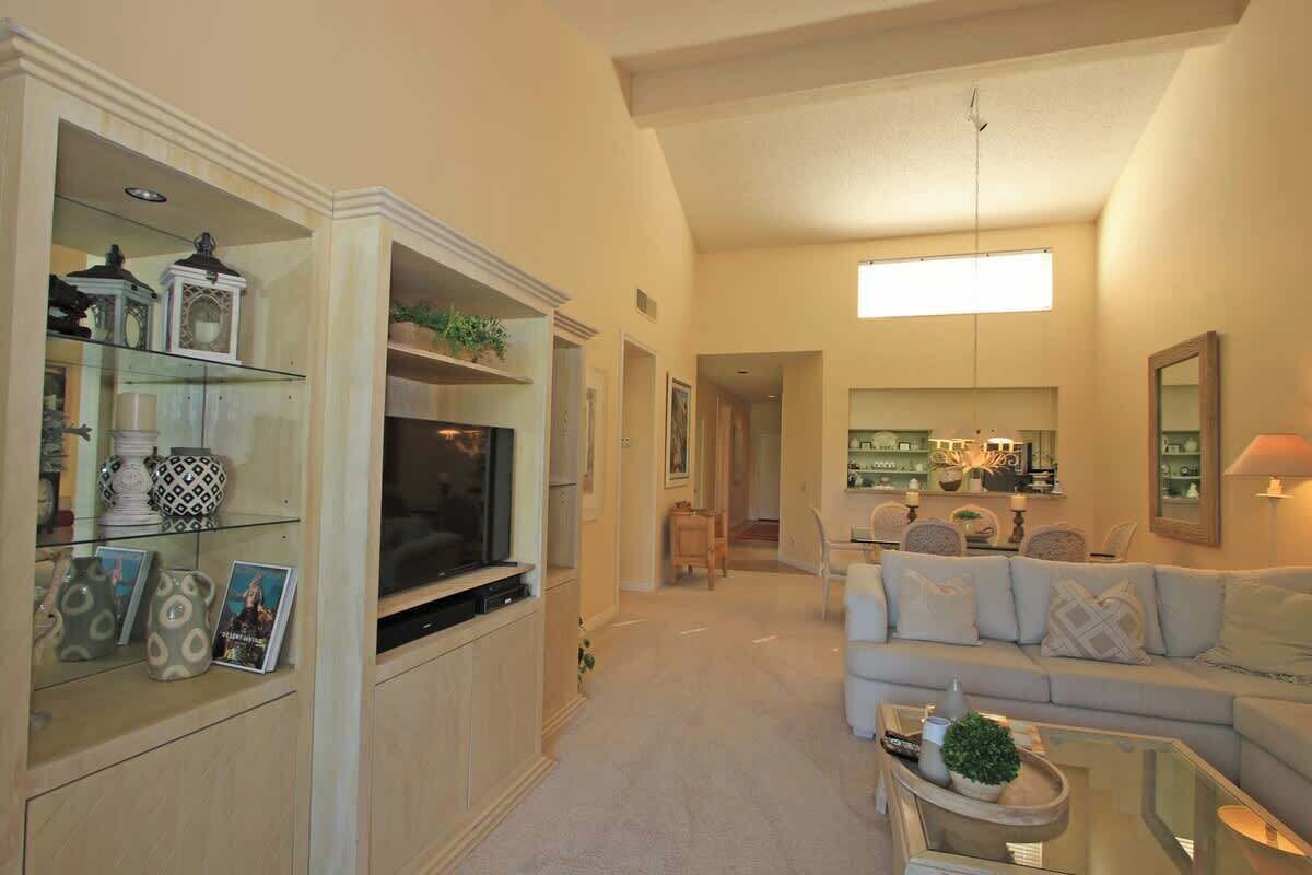 A spacious living room with a large TV, a sofa, and a coffee table. There is a kitchen area in the background with a dining table and chairs.
