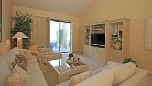 A living room with a sofa, coffee table, and TV stand. There is a sliding glass door leading to an outdoor area. - Moutain and Fairway Views-Walk to Pool-V3986 (Palm Desert)