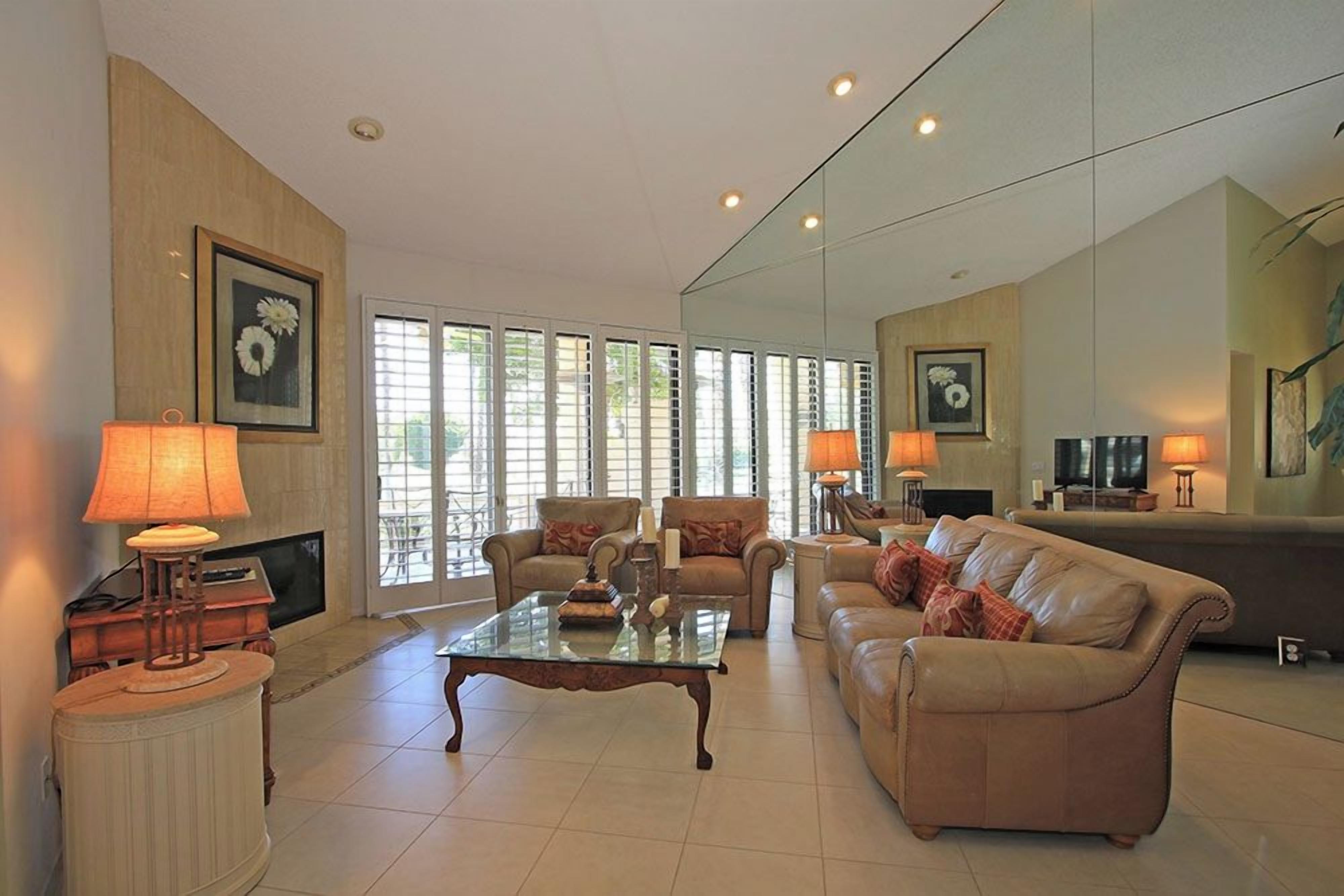 Step into your sunlit living space where a plush leather sofa welcomes you to unwind. Natural light pours through plantation shutters, illuminating the elegant details and warm ambiance of your retreat.