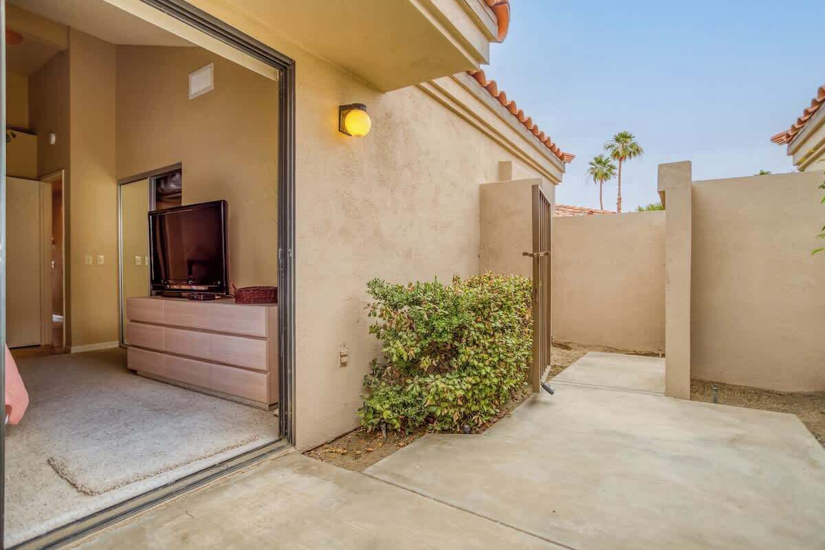A residential entryway with a sliding glass door, a beige wall, a small garden, and a light fixture.