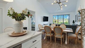 Una cucina moderna con un piano di lavoro in marmo, un vaso con fiori e una zona pranzo con sedie e tavolo in legno.