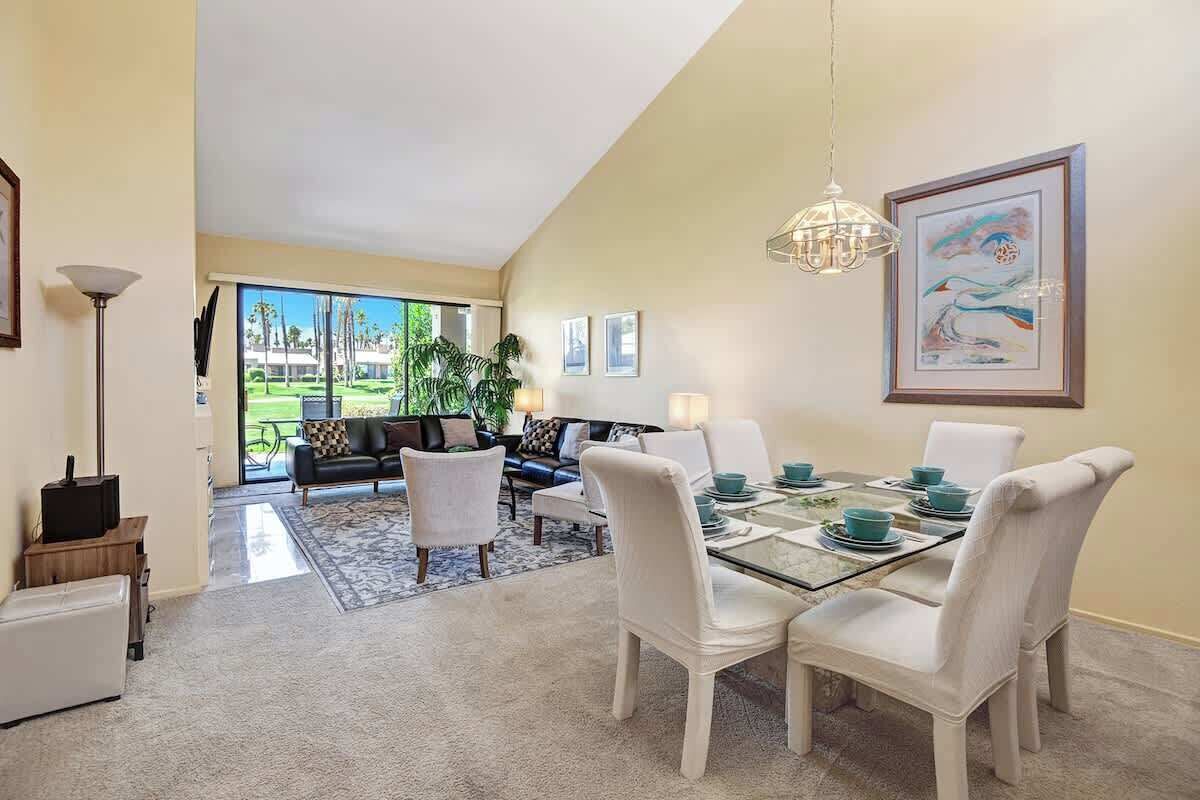 A dining area with a glass table, white chairs, teal tableware, and a chandelier.