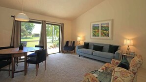 A living room with a dining table, sofa, and chairs, a large window with curtains, and a painting on the wall. - Condo with views, BBQ|Pool, golf, tennis access (Palm Desert)