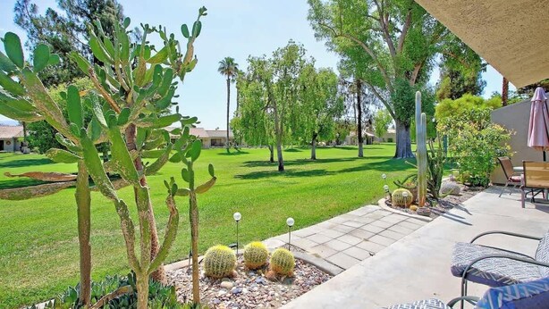 A patio area with a cactus plant, outdoor furniture, and a well-maintained lawn. - Condo with views, BBQ|Pool, golf, tennis access (Palm Desert)